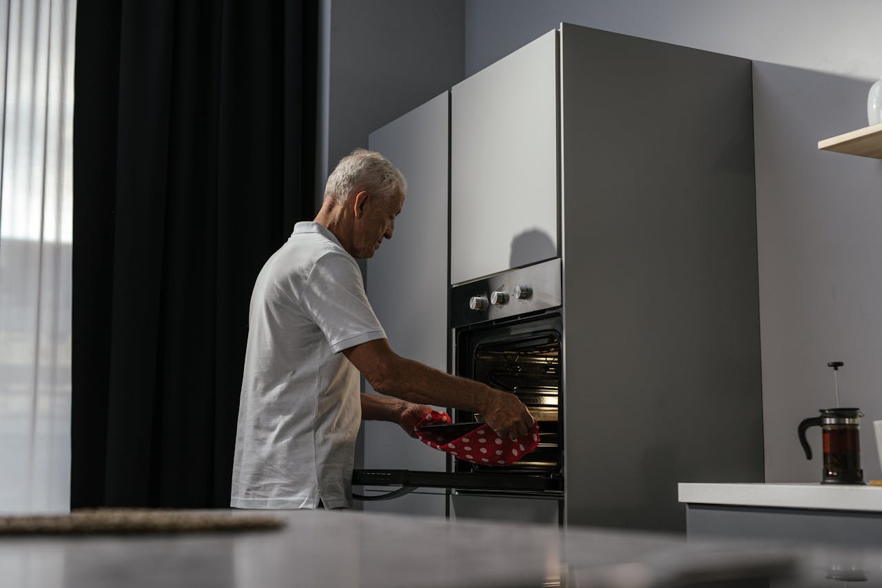 about-us Elderly man using oven in a modern kitchen interior with a focus on light and shadows.