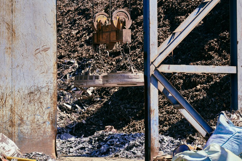pexels-photo-36397933-36397933 Magnetic crane sorting metal in an industrial scrapyard. Bright daylight highlights the steel and machinery.